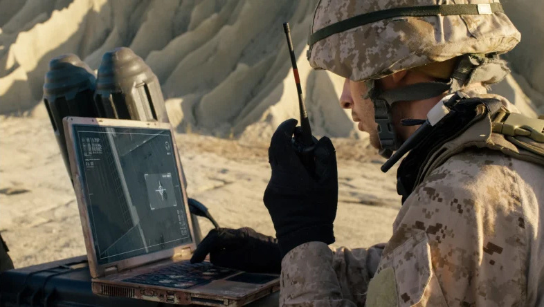  US military soldier in desert camo operating portable computer and walkie talkie in desert environment